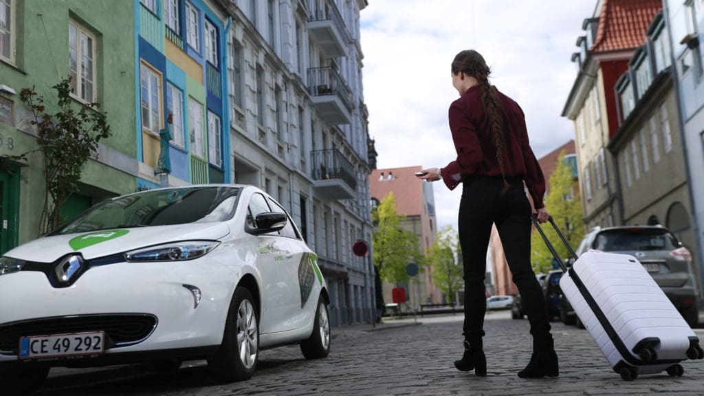 Girl with suitcase walking towards a GreenMobility car