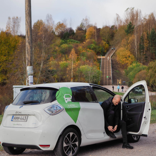 man in car ties his shoe with an autumn forest in the background