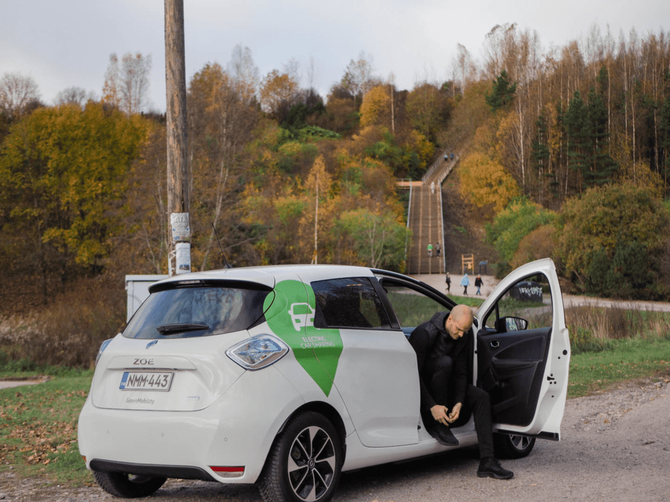 man in car ties his shoe with an autumn forest in the background