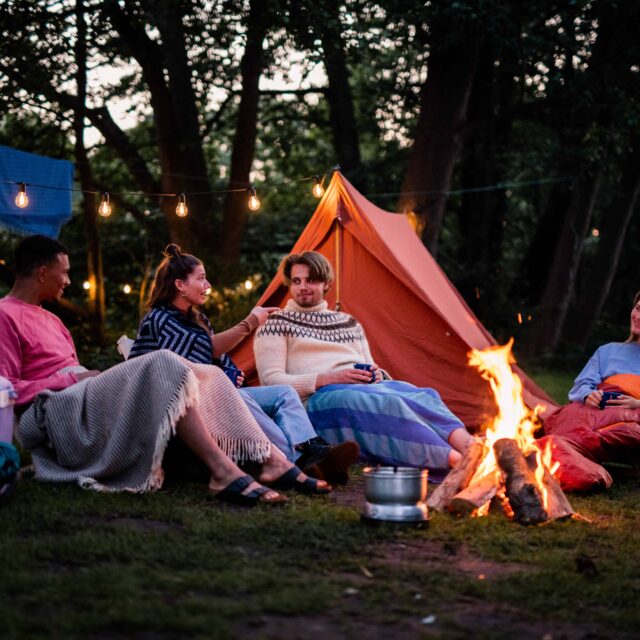 Unge mennesker sidder omkring et bål på en glamping